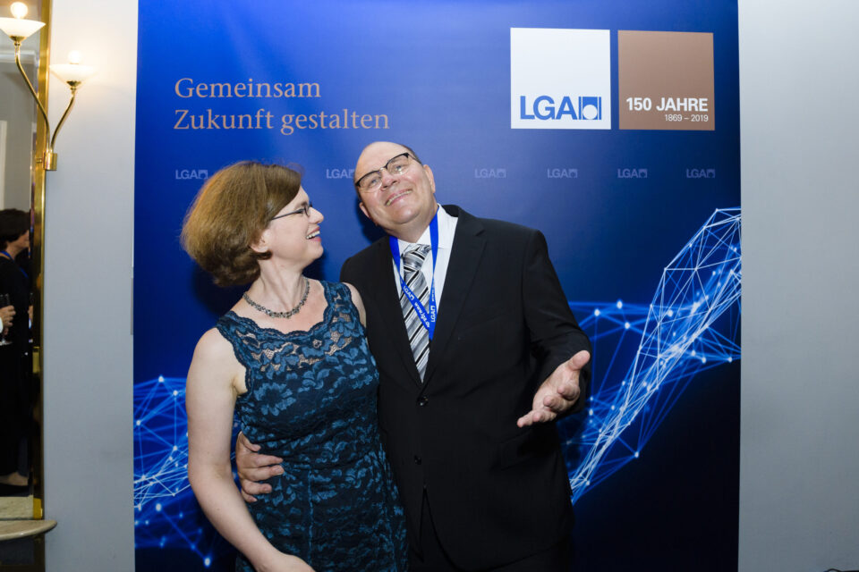 Das Bild zeigt zwei Personen, die vor einem blauen Hintergrund posieren. Auf dem Hintergrund steht der Schriftzug „Gemeinsam Zukunft gestalten“ sowie das LGA Logo 150 Jahre