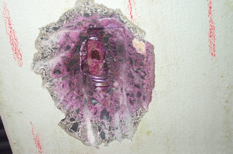 Nahaufnahme einer Wandstruktur mit unregelmäßigen violetten, rosafarbenen und rötlichen Farbverläufen; die Oberfläche wirkt rau und stellenweise fleckig.