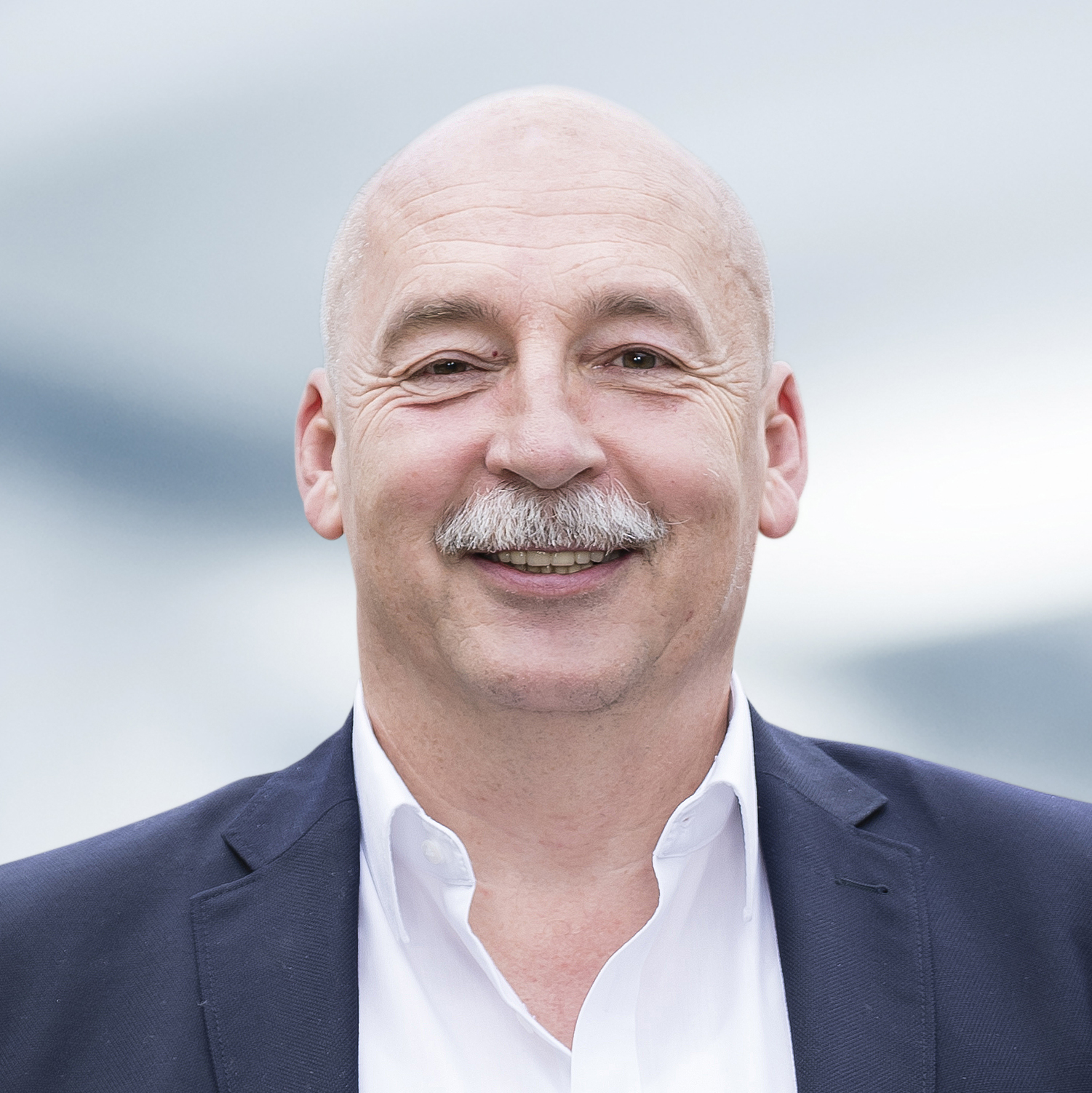 Dieter Straußberger trägt ein weißes Hemd und ein dunkles Sakko. Der Hintergrund ist unscharf und zeigt ein Büro.