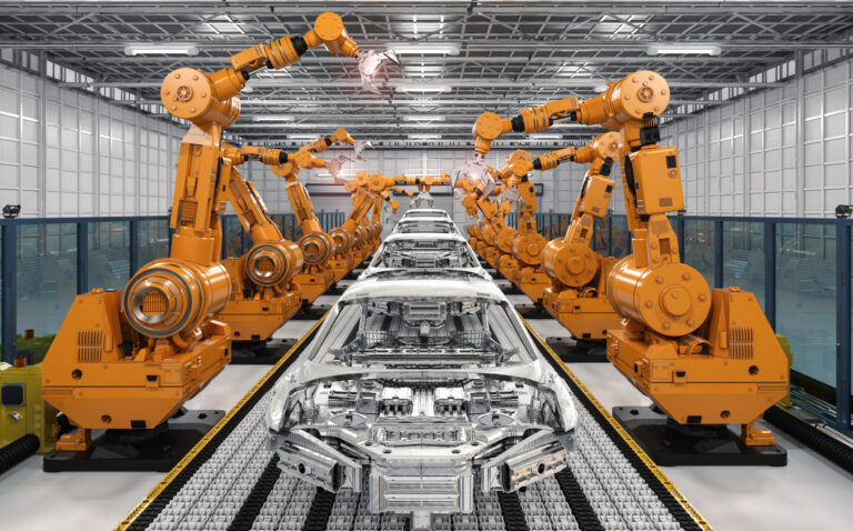Das Bild zeigt eine Automobilfertigungsstraße mit mehreren orangefarbenen Roboterarmen, die an Karosserierahmen arbeiten. Die Roboterarme sind beidseitig entlang eines Förderbands angeordnet, das die Fahrzeugrahmen durch den Montageprozess transportiert. Die Umgebung ist eine große, gut beleuchtete Industriehalle mit hoher Decke und gitterartiger Struktur.