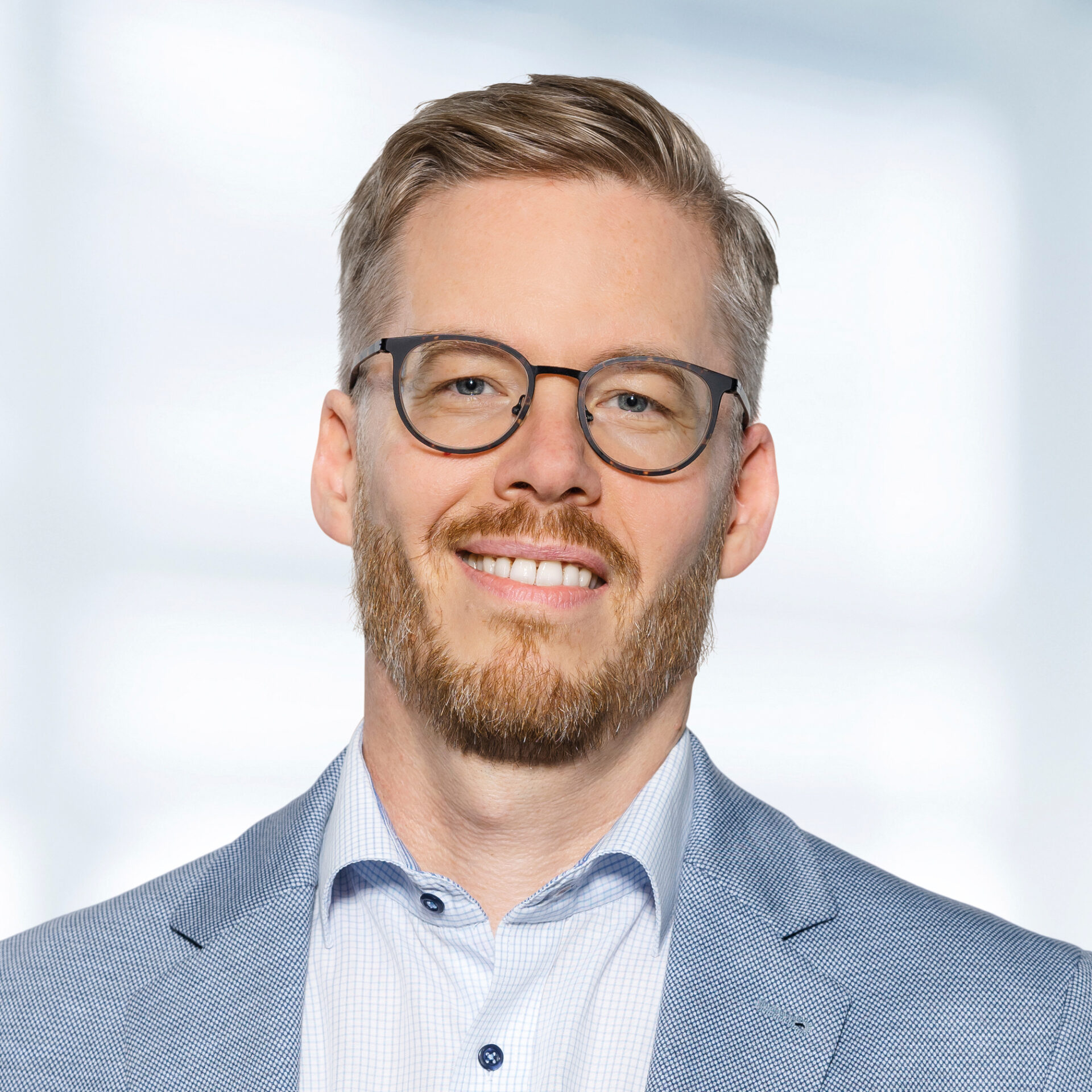 Marko Gehlhaar trägt ein hellblaues Sakko und ein hellblau kariertes Hemd. Der Hintergrund ist unscharf und zeigt ein Büro.