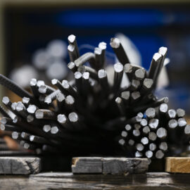 Auf dem Bild sind mehrere zugeschnittene Betonstahlstäbe zu sehen, die gebündelt auf einer Arbeitsfläche liegen. Die Stirnseiten der Stäbe sind im Vordergrund deutlich sichtbar und zeigen unterschiedliche Durchmesser. Durch die geringe Tiefenschärfe hebt sich das Material klar vom unscharfen Hintergrund einer Werkstatt oder Produktionsumgebung ab.
