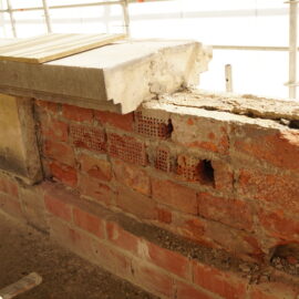 Teilweise freigelegtes Mauerwerk mit beschädigten Ziegeln und Betonauflager als Beispiel für Bauschäden im Bestand.