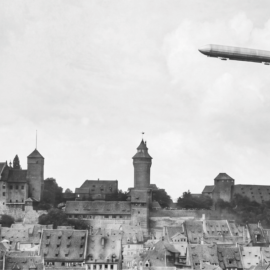 Historische Schwarz-Weiß-Aufnahme der Nürnberger Kaiserburg mit einem Zeppelin am Himmel – Sinnbild für die Entstehung des Namens „Zeppelinfeld“.