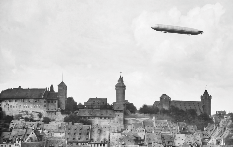 Historische Schwarz-Weiß-Aufnahme der Nürnberger Kaiserburg mit einem Zeppelin am Himmel – Sinnbild für die Entstehung des Namens „Zeppelinfeld“.