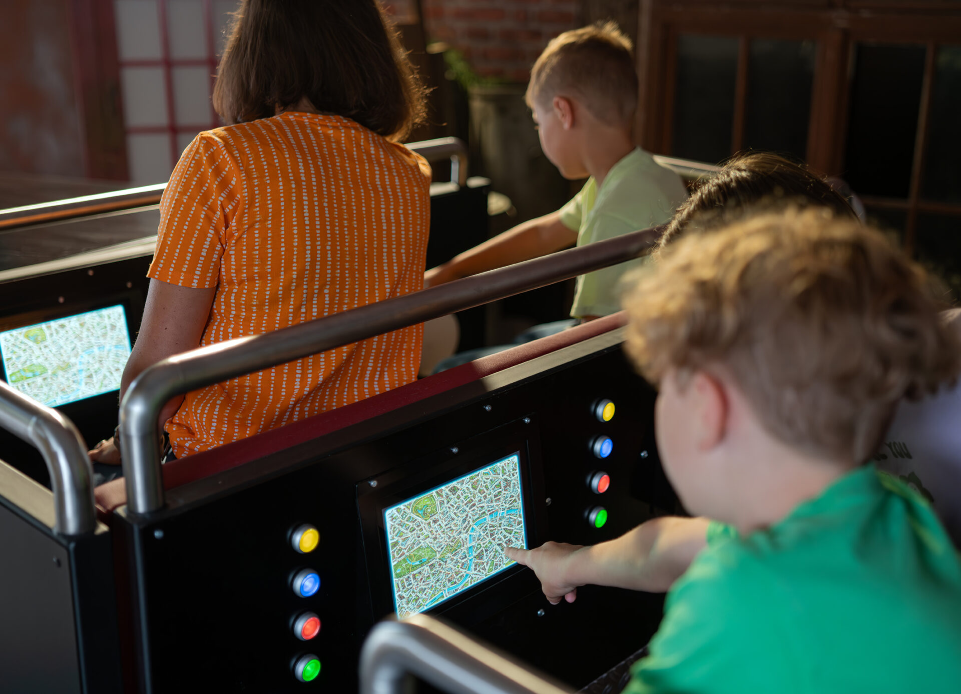 > Kinder sitzen in den Fahrzeugen der Fahrattraktion „Scotland Yard Ride“ und bedienen über integrierte Touchscreens eine digitale Karte, die während der Fahrt zur Orientierung und Interaktion dient.