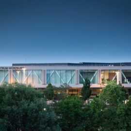 Congress Centrum Würzburg, modernes Gebäude mit großen Glasfenstern und elegantem Design, umgeben von Bäumen und beleuchtet von Straßenlaternen in den frühen Morgen- oder Abendstunden.