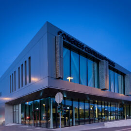 Modernes Gebäude mit der Aufschrift CONGRESS CENTRUM WÜRZBURG an der Fassade, mit großen Glasfenstern und zeitgemäßem Design; aufgenommen in der Dämmerung oder am frühen Abend, beleuchtet von Straßenlaternen.
