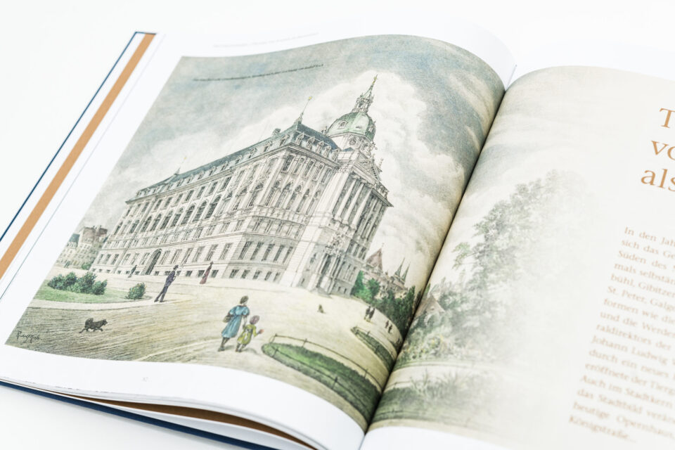 Das Bild zeigt ein aufgeschlagenes Buch mit einer Illustration eines großen historischen Gebäudes mit klassischer Architektur und einer markanten Kuppel. Im Vordergrund sind mehrere Personen und ein kleiner Hund zu sehen. Auf der rechten Seite befindet sich ein Text in deutscher Sprache.