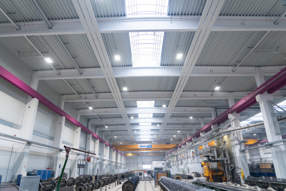 Innenraum einer großen Industriehalle mit hohen Decken, Oberlichtern, mehreren großen zylindrischen Objekten und sichtbaren Hallenkränen, genutzt als Fertigungs- oder Montagebereich.