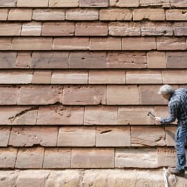 Eine Person mit kariertem Hemd inspiziert die Nürnberger Stadtmauer und untersucht die Steinstruktur mit einem Hammer.