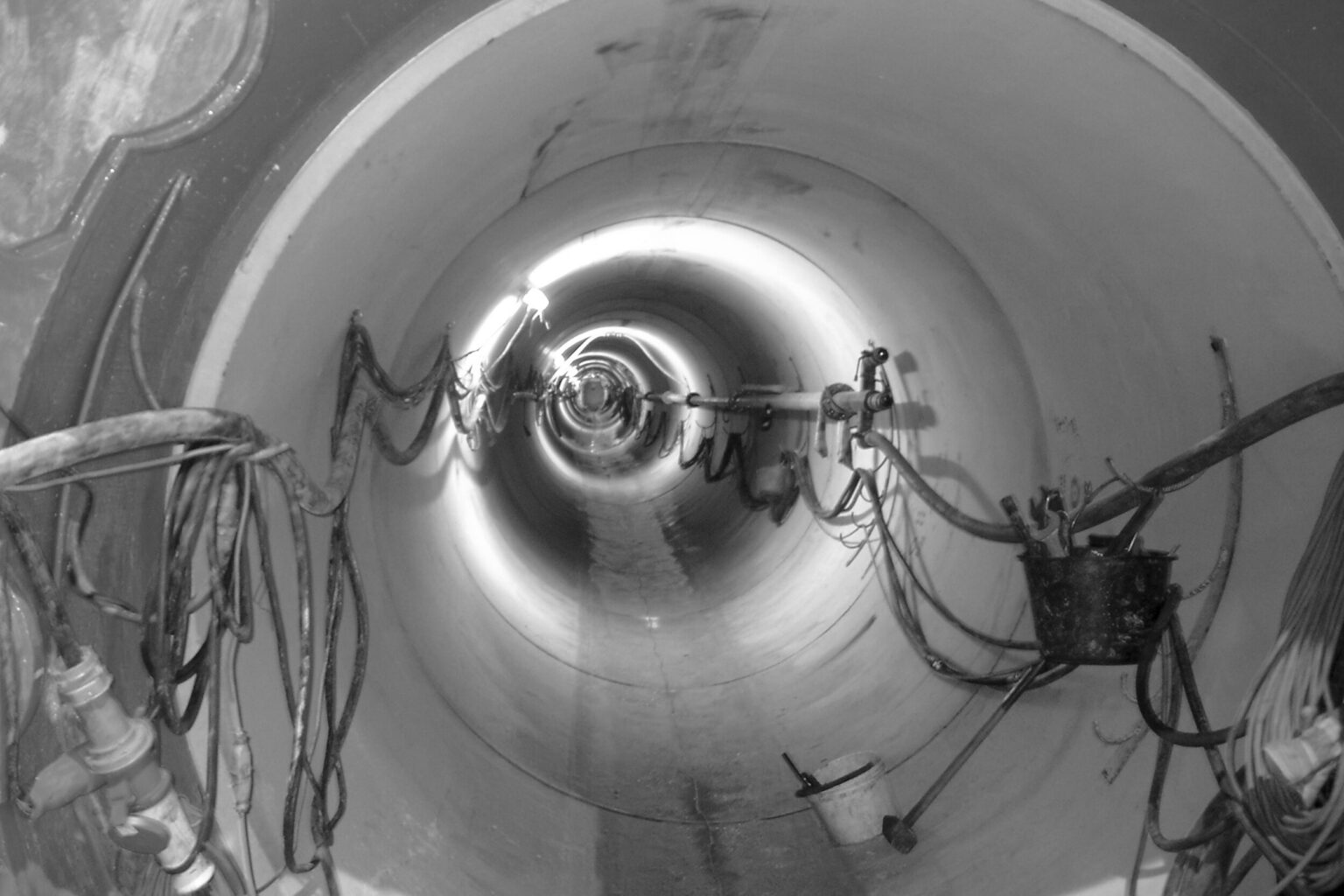 Innenansicht eines großen, beleuchteten Rohr- oder Tunnelsystems mit entlang der Wände verlaufenden Kabeln und technischen Vorrichtungen.