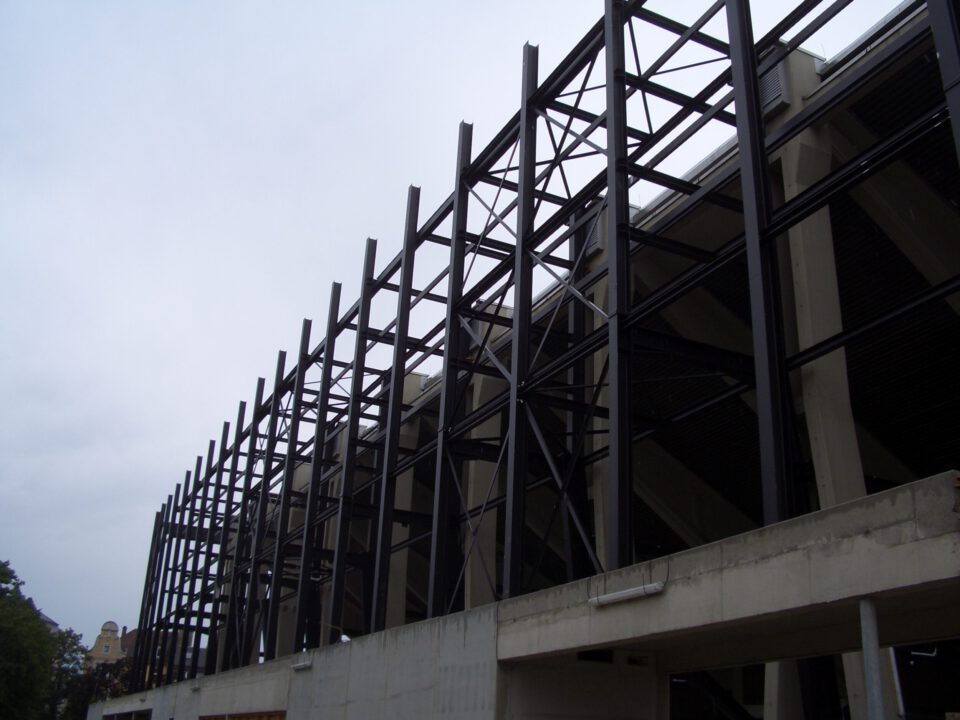 Teilweise errichtetes Gebäude mit sichtbarem Stahlrahmen aus vertikalen und horizontalen Trägern in Gitterstruktur; der untere Bereich besteht aus Beton, der obere aus Stahlkonstruktion.