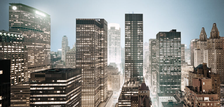 Das Bild zeigt eine Stadtansicht mit zahlreichen hohen Gebäuden und Wolkenkratzern, die dicht beieinander stehen. Viele Fenster sind beleuchtet, was auf frühen Morgen oder Abend hindeutet. Der Himmel ist klar und die Szene vermittelt den Eindruck einer lebendigen Großstadt.