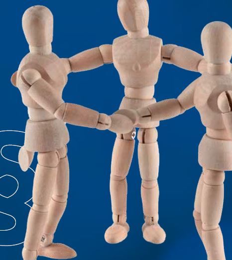 Das Bild zeigt drei hölzerne Künstlerfiguren, die im Kreis stehen und sich an den Händen halten. Der Hintergrund ist einfarbig blau.