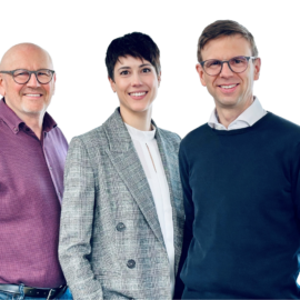 Das Bild zeigt drei Personen, die nebeneinander vor einem weißen Hintergrund stehen. Die linke Person trägt ein lila-kariertes Hemd und Jeans, die mittlere einen grauen Blazer mit Muster über einem weißen Hemd, und die rechte Person eine Brille sowie einen dunkelblauen Pullover über einem weißen Hemd.