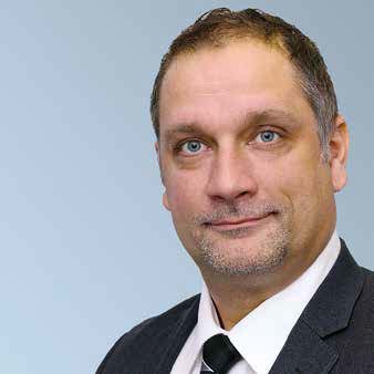 Das Bild zeigt eine Person in Anzug und Krawatte vor einem einfarbig hellblauen Hintergrund.