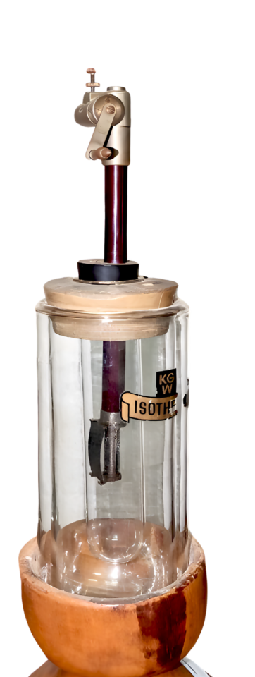 Das Bild zeigt ein Laborgerät mit einem gläsernen Behälter, der auf einem Holzsockel steht und oben ebenfalls mit Holz eingefasst ist. Im Inneren befindet sich eine Metallstange, die mit einem verstellbaren Armmechanismus am oberen Teil verbunden ist.