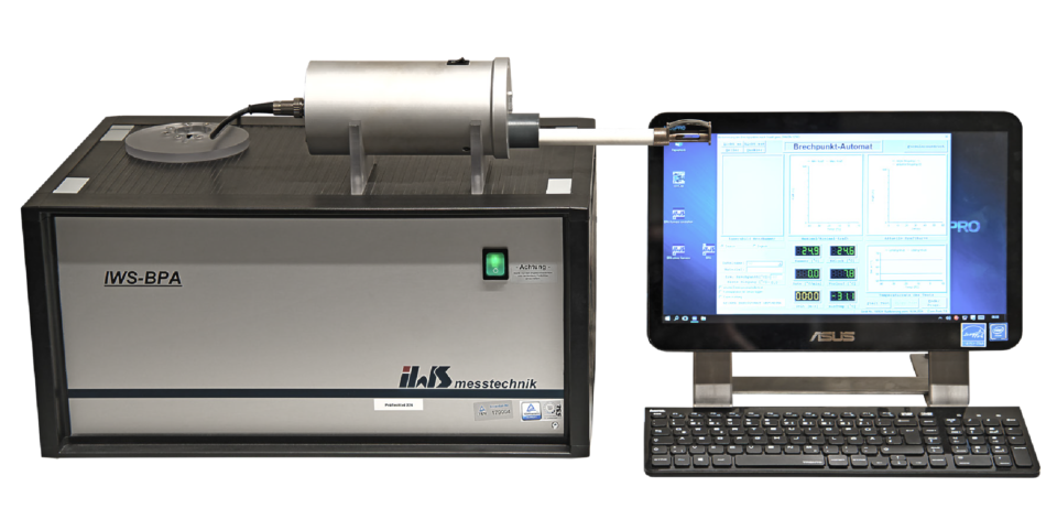 Das Bild zeigt ein Laborgerät vom Typ IWS-BPA, das mit einem Monitor und einer Tastatur verbunden ist. Auf dem Bildschirm ist eine Software mit verschiedenen Diagrammen und Datenfeldern zu sehen. Das Gerät besitzt ein zylindrisches Bauteil, das über ein Kabel mit der Haupteinheit verbunden ist.