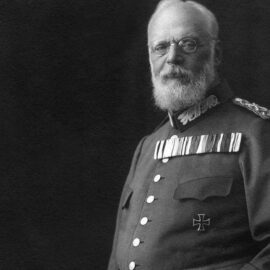 Historische Schwarz-Weiß Fotografie von König Ludwig III. in Militäruniform mit zahlreichen Orden und Auszeichnungen vor dunklem Hintergrund.