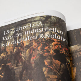 Das Bild zeigt ein aufgeschlagenes Buch mit einer Illustration und Text auf der linken Seite. Der Text lautet: 150 Jahre LGA. Von der industriellen zur digitalen Revolution. Die rechte Seite ist nicht vollständig sichtbar.