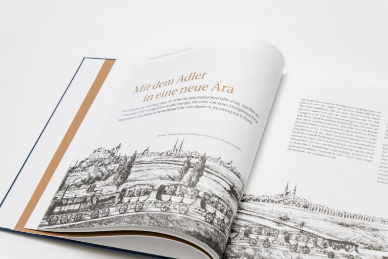 Das Bild zeigt ein aufgeschlagenes Buch mit Text und Illustrationen über beide Seiten. Es wird die Jungfernfahrt der ersten deutschen Eisenbahn von Nürnberg nach Fürth im Jahr 1835 beschrieben.