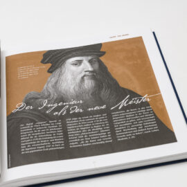 Das Bild zeigt ein aufgeschlagenes Buch mit einer Schwarz-Weiß-Fotografie von Industrieanlagen auf der linken Seite. Die rechte Seite enthält eine Illustration einer Person mit langem Haar und Hut sowie den Titel „Der Ingenieur als der neue Meister“.