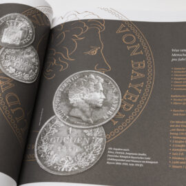 Das Bild zeigt ein aufgeschlagenes Buch mit dunklem Hintergrund und mehreren Abbildungen historischer Münzen. Auf der linken Seite sind zwei große Münzen mit feinen Gravuren zu sehen, auf der rechten Seite eine weitere Münze mit einem Profilporträt und der Aufschrift „VON BAYERN“. Daneben befindet sich ein Text mit historischen Gehaltsangaben verschiedener Berufe.