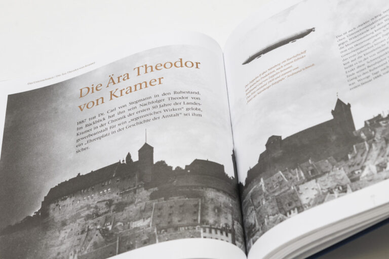 Das Bild zeigt ein aufgeschlagenes Buch mit einer Schwarz-Weiß-Fotografie einer Burg oder Festung auf einem Hügel auf der linken Seite. Daneben steht ein Text über die Ära Theodor von Kramer. Auf der rechten Seite ist ein Luftschiff (Zeppelin) abgebildet, begleitet von weiterem Text.