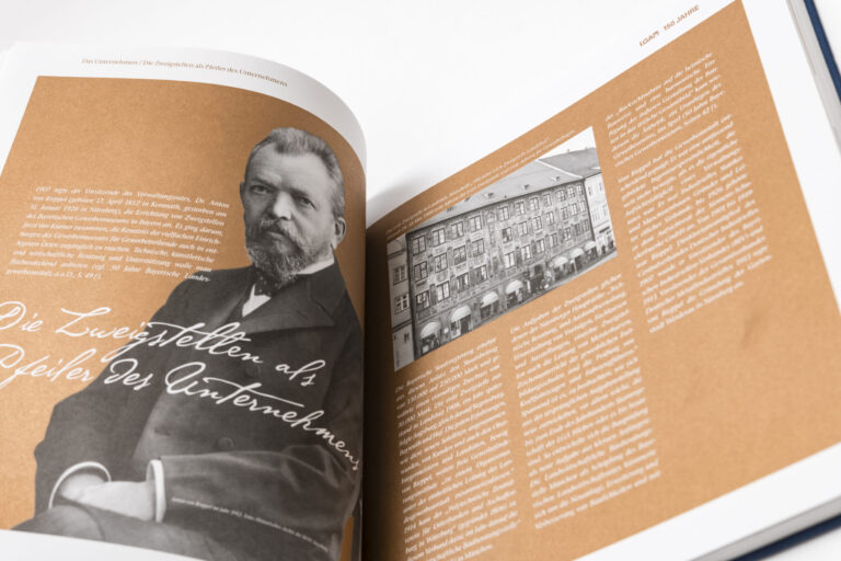 Das Bild zeigt ein geöffnetes Buch mit zwei sichtbaren Seiten. Auf der linken Seite ist ein schwarz-weißes Foto eines Mannes sowie ein deutscher Text zu sehen. Die rechte Seite zeigt ein weiteres schwarz-weißes Foto eines Gebäudes und ebenfalls deutschen Text.