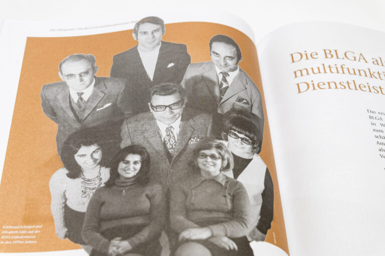 Das Bild zeigt eine Seite aus einem Buch oder Magazin mit einer alten schwarz-weißen Fotografie von acht Personen. Die Gruppe besteht aus fünf Männern und drei Frauen in formeller Kleidung, typisch für die Mitte des 20. Jahrhunderts. Der Hintergrund ist orange eingefärbt.