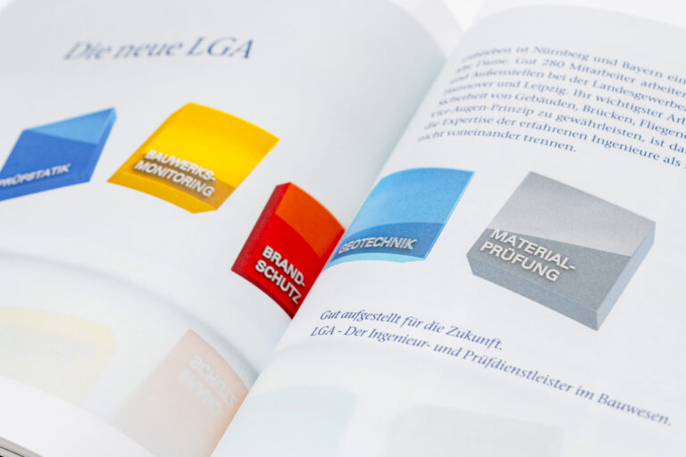 Das Bild zeigt ein geöffnetes Buch mit farbigen 3D-Blöcken auf der linken Seite, die verschiedene Kategorien darstellen. Die Blöcke sind mit Begriffen wie „PRÜFSTATIK“, „BAUWERKSMONITORING“, „BRANDSCHUTZ“, „GEOTECHNIK“ und „MATERIALPRÜFUNG“ beschriftet. Auf der rechten Seite befindet sich ein deutscher Textabschnitt mit einer Einleitung zur zukünftigen Ausrichtung der LGA im Bauwesen.