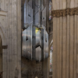 Innenraum einer großen Kathedrale mit hohen, verzierten Säulen und Bögen; im Mittelpunkt eine große Orgel mit zahlreichen Metallpfeifen, im Hintergrund bunte Glasfenster und architektonische Details.
