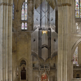 Innenraum einer großen Kathedrale mit hohen Gewölbedecken und bunten Glasfenstern; im Mittelpunkt eine große Orgel mit zahlreichen Metallpfeifen über dem Altar.