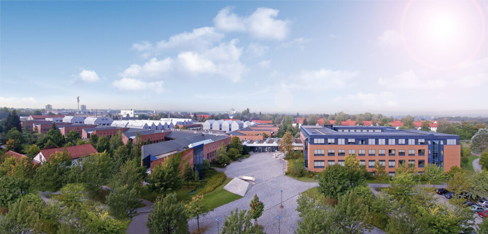 Panorama Luftbild des LGA Gebäudekomplexes umgeben von Bäumen und Grünflächen bei sonnigem Wetter.