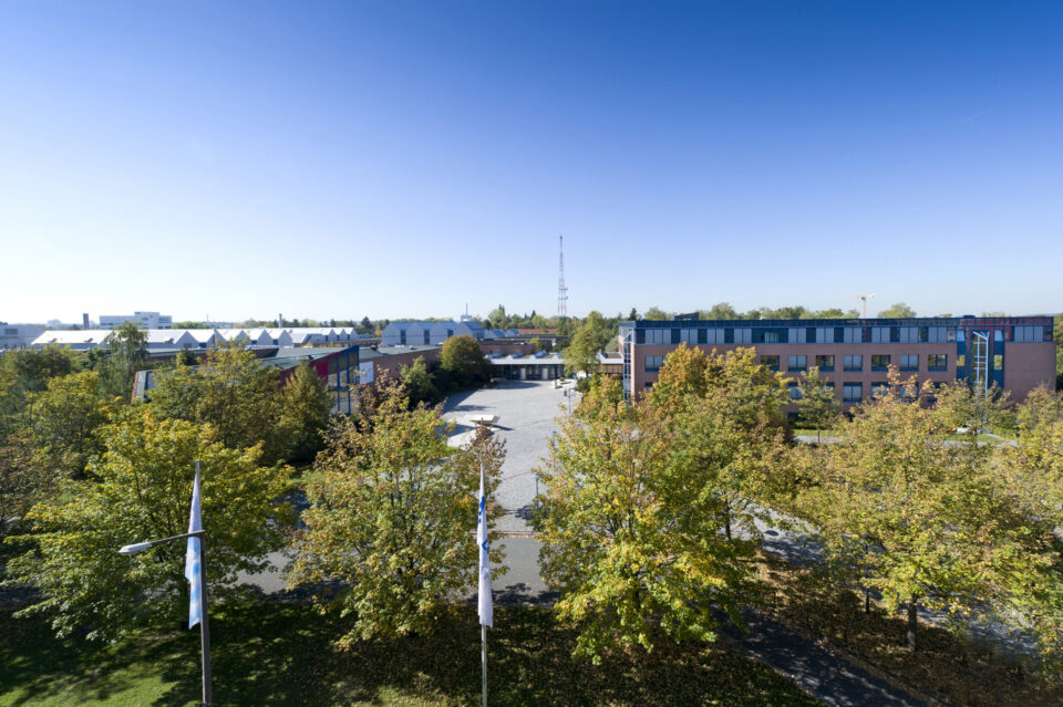 Luftaufnahme des LGA-Gebäudes in Nürnberg mit mehreren Gebäuden, im Vordergrund Bäume von der Sonne angestrahlt.