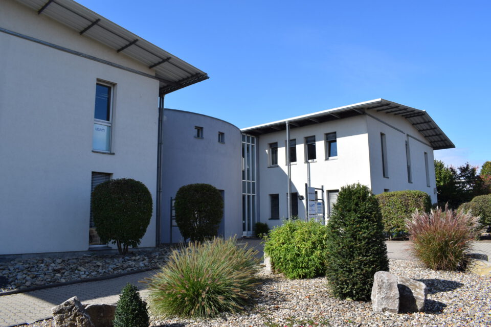 Moderner Bürokomplex mit zwei Gebäuden in zeitgemäßem Design, großen Fenstern und flachen Dächern sowie umliegender Begrünung bei sonnigem Wetter.