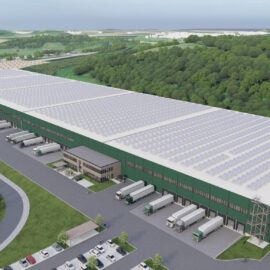 Das Bild zeigt ein grafisches 3D Modell eines großen Industrie- oder Logistikzentrum mit grünem Außenanstrich, zahlreichen Laderampen, parkenden Lkw, einem mit Solarpanels bedeckten Dach sowie umliegenden Parkplätzen, Straßen und Grünflächen.