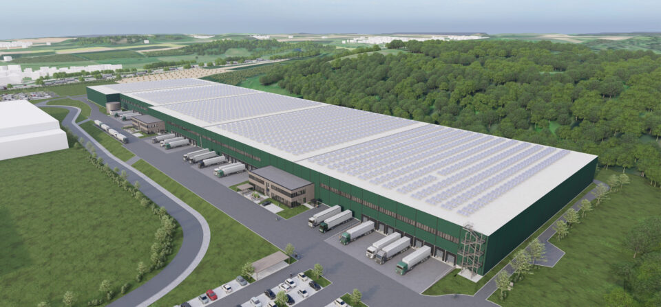 Das Bild zeigt ein grafisches 3D Modell eines großen Industrie- oder Logistikzentrum mit grünem Außenanstrich, zahlreichen Laderampen, parkenden Lkw, einem mit Solarpanels bedeckten Dach sowie umliegenden Parkplätzen, Straßen und Grünflächen.